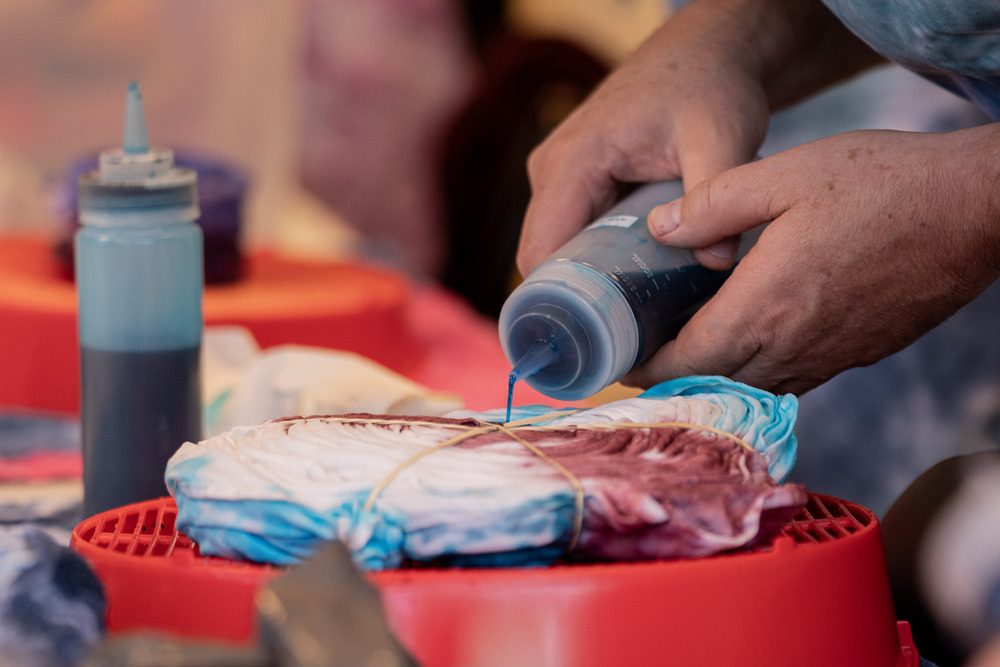 En person färgar en hopvikt tygbit med blå och lila färg för att skapa batikmönster.