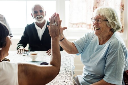 Äldre personer sitter och fikar runt ett bord. Två personer hälsar på varandra med en high five.