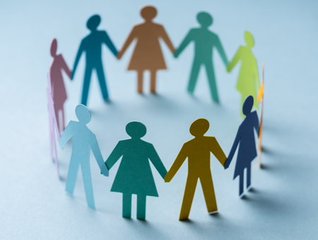 Pappersfigurer i olika färger håller varandra i händerna och bildar en cirkel på ett ljusblått underlag.