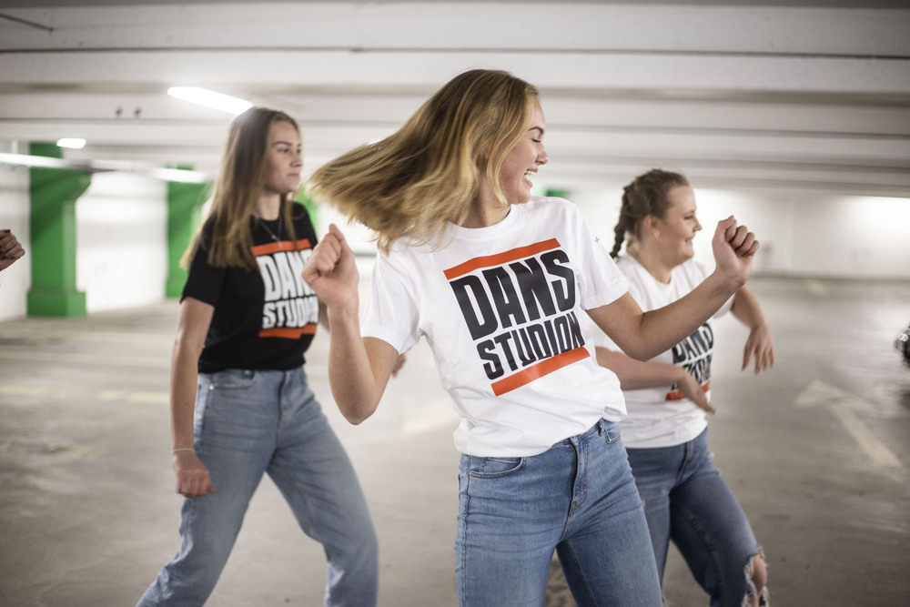 Tre dansare i parkeringsgarage i Dansstudion-tröjor