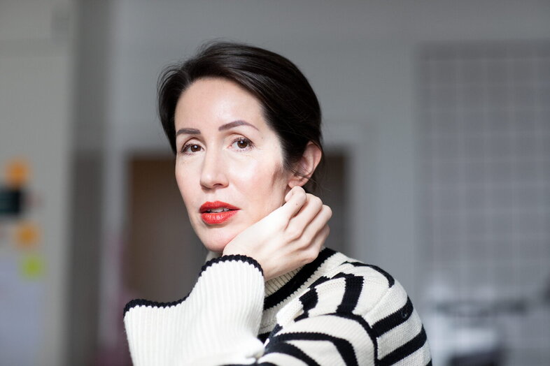 Kvinna med mörkt hår och röd läppstift bär en randig tröja och tittar in i kameran.