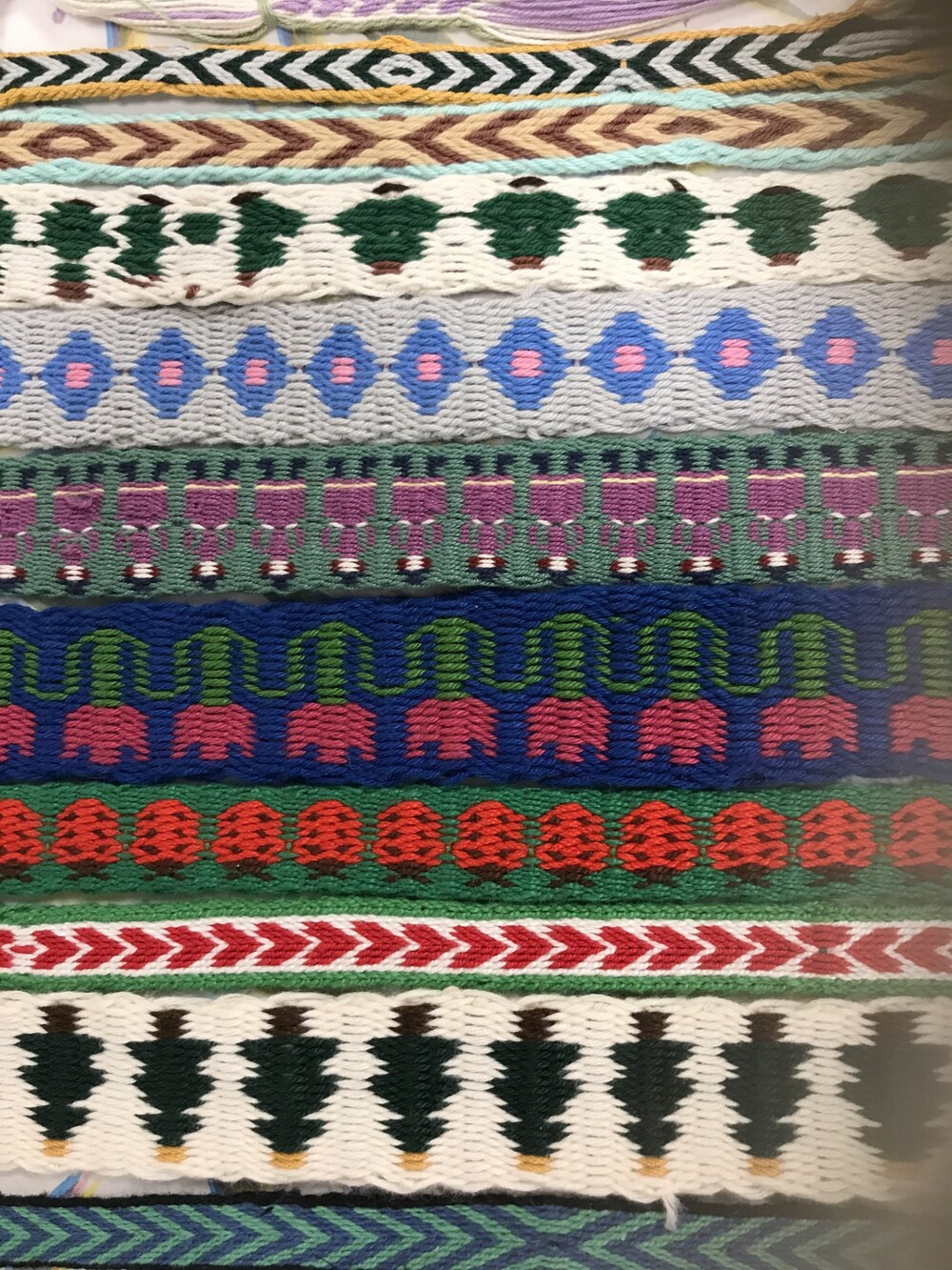 Färgglatt vävt tyg med mönster av träd, blommor och stiliserade människor i rader.