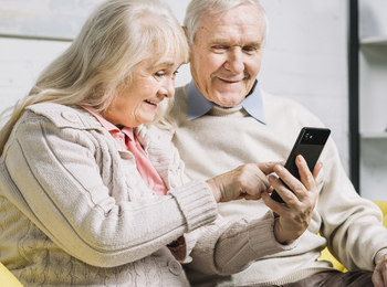 Ett äldre par sitter tillsammans i en soffa och tittar leende på en smartphone.