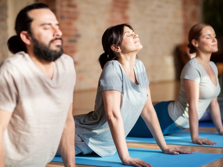 Tre personer gör en yogaövning på blå mattor inomhus, med ansiktena vända uppåt och ögonen slutna.