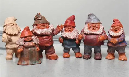 Sex små tomteliknande figurer i olika färger står uppradade mot en grå bakgrund.
