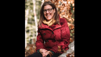 Person med röd kappa och gul halsduk sitter utomhus bland höstlöv.