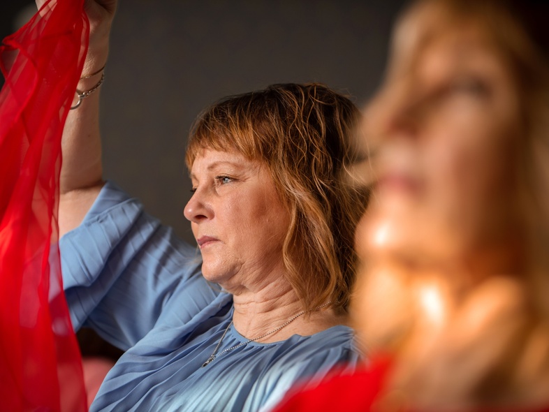 Kvinna i blå tröja håller upp ett rött tygstycke, med en annan kvinna suddigt i förgrunden.