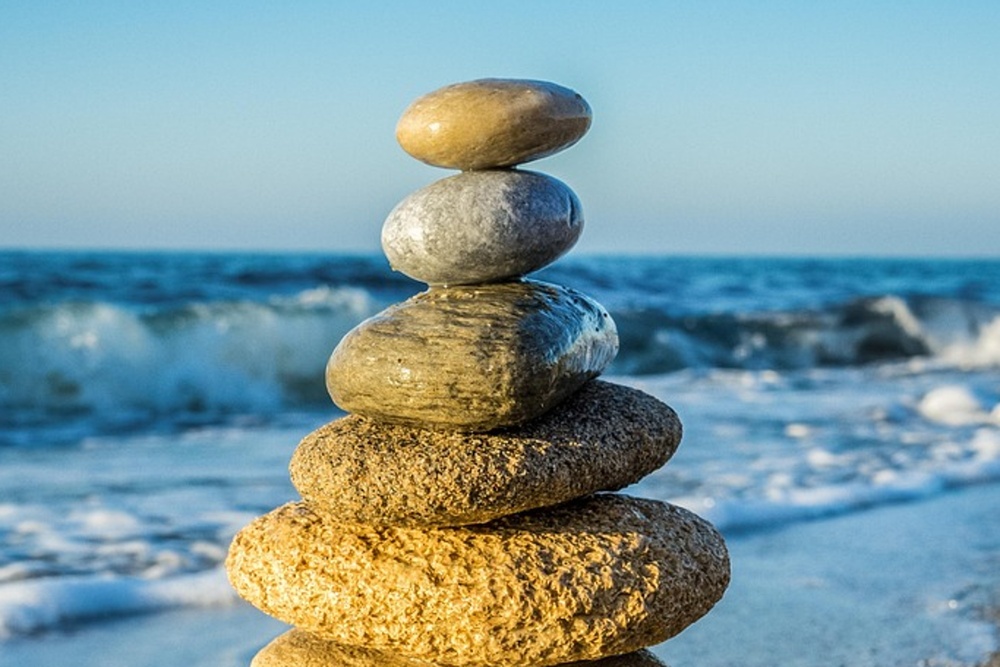 Stapel av stenar på en sandstrand med havsvågor i bakgrunden under klarblå himmel.