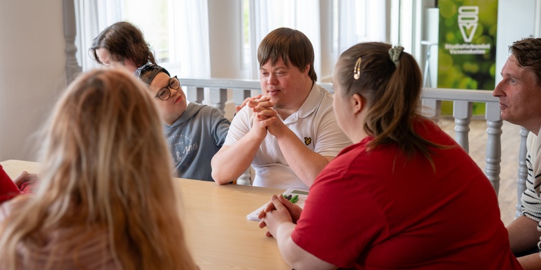 En grupp personer sitter runt ett bord och samtalar i ett ljust rum.