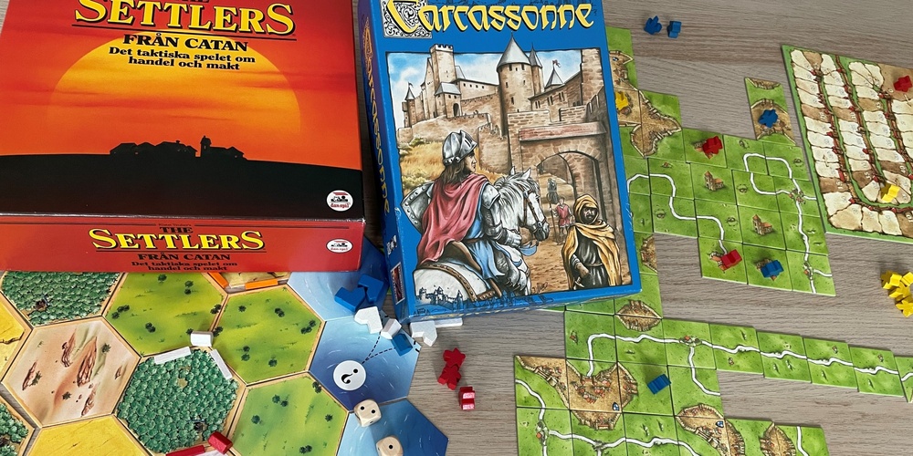 Två sällskapsspel, Settlers från Catan och Carcassonne, uppdukade på ett bord med spelbrickor och pjäser.