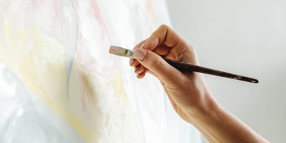 En hand målar på en duk med en pensel, palett med färg syns i förgrunden.