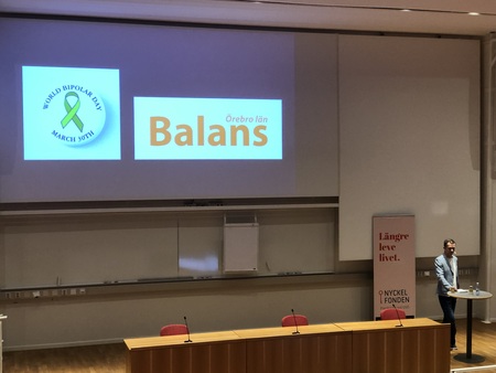 Föreläsningssal med presentation om bipolär sjukdom, en person står vid ett podium.