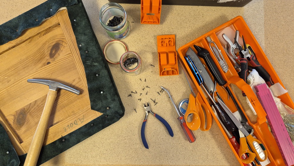Arbetsbänk med verktyg, skruvar, hammare och en träskiva med tyg, redo för möbelrenovering.
