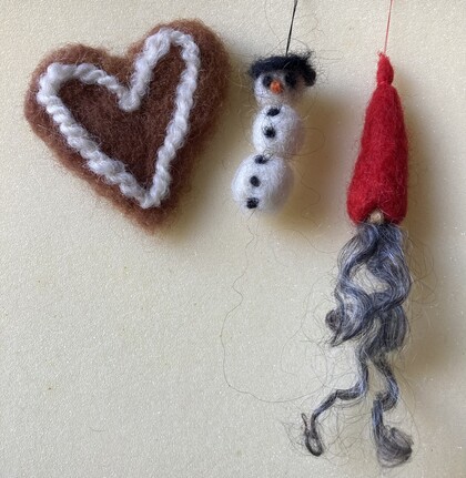 Tre tovade ullfigurer: ett hjärta, en snögubbe och en tomte med lång skägg på ljus bakgrund.