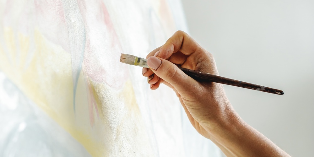 En hand målar på en duk med en pensel, palett med färg syns i förgrunden.