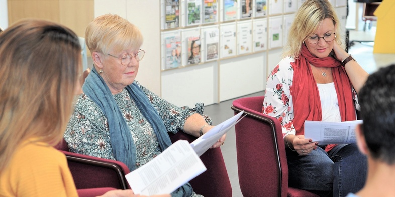 Fyra personer sitter i en cirkel och läser papper i ett ljust rum, troligen under ett möte eller en studiecirkel.