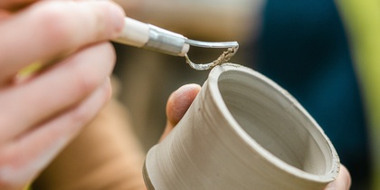 En person dekorerar en lerkruka med ett verktyg i en keramikverkstad.