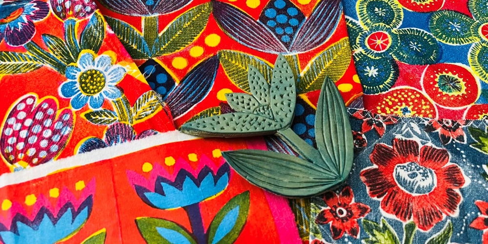 Färgglada tyger med blommönster och två gröna bladformade stämplar ovanpå.