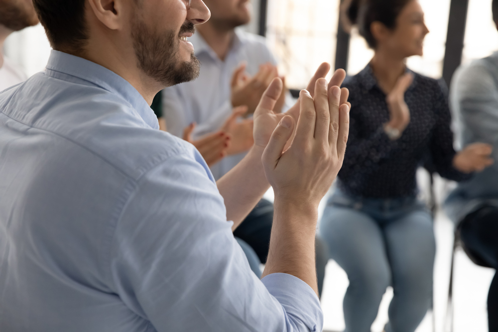 Flera personer sitter i en grupp och applåderar, fokus på händer och överkroppar.