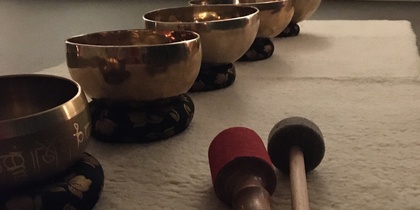 Fem tibetanska klangskålar står på rad på en matta med två klubbor framför dem i ett dämpat rum.