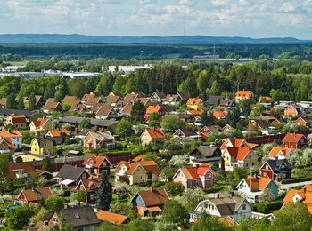 Färgglada villor med röda och gula tak i ett lummigt bostadsområde, omgivna av skog och berg i bakgrunden.