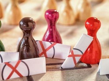 Färgade spelpjäser står i en grupp omgivna av barriärer med röda kryss, fler pjäser i bakgrunden.