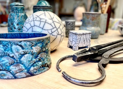 Keramikföremål i blått och vitt med krackelerad glasyr står på ett träbord tillsammans med en tång.