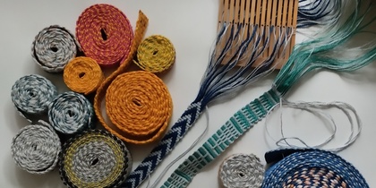Olika färgglada band och snoddar, samt vävredskap, ligger utspridda på ett vitt underlag.
