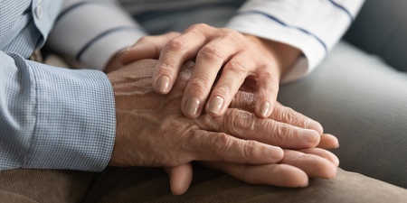 Två personer håller varandra i händerna, en gest av stöd och närhet.