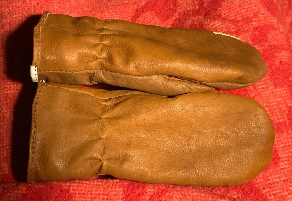 Ett par bruna lädervantar ligger på en röd tygbakgrund.