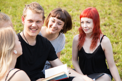 Fyra unga vuxna sitter på gräset och samtalar, två av dem håller böcker i händerna.