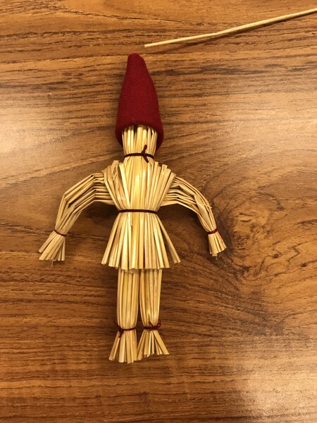 En figur gjord av halm med röd luva ligger på ett träbord.