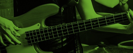 Två kvinnor spelar elbas och trummor på en scen, bilden har ett grönt filter.