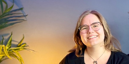 Två leende personer sitter tillsammans i en blå soffa i ett rum med blå vägg och grön växt.