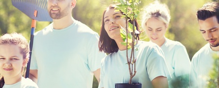 Fyra unga vuxna och ett barn planterar träd tillsammans utomhus en solig dag.