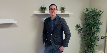 En person står vid väggen i ett mötesrum med bord, stolar, växter och hyllor med krukväxter.