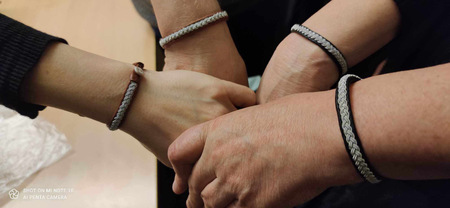 Fyra händer med likadana armband håller i varandra i en cirkel.