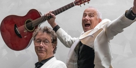 Två personer i vita kavajer, en håller trumpet och den andra hoppar med en gitarr mot en ljus bakgrund.