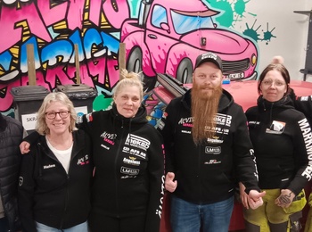 Sex personer står framför en röd bil i ett garage med färggraffiti på väggen.