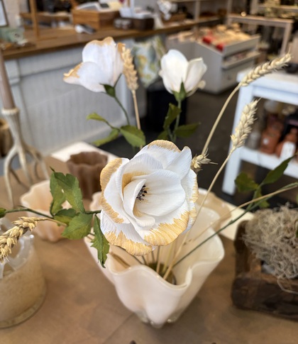 Vita konstgjorda blommor med gula kanter i en vit vas på ett bord i en butiksmiljö.