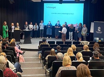 Sittande publik och ett antal personer på scen. Konferensmiljö.