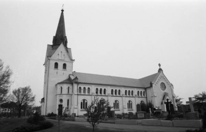 Svartvit bild på en kyrka med högt torn och gravstenar i förgrunden.
