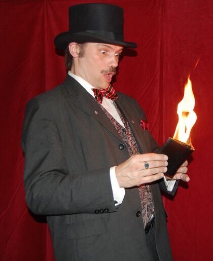 Man i kostym och hög hatt håller en plånbok med eldslåga, ser förvånad ut mot röd bakgrund.