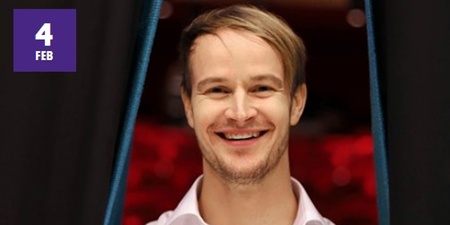 Leende man med ljust hår står mellan två svarta draperier, bakgrund i rött. Datumet 4 februari syns i hörnet.