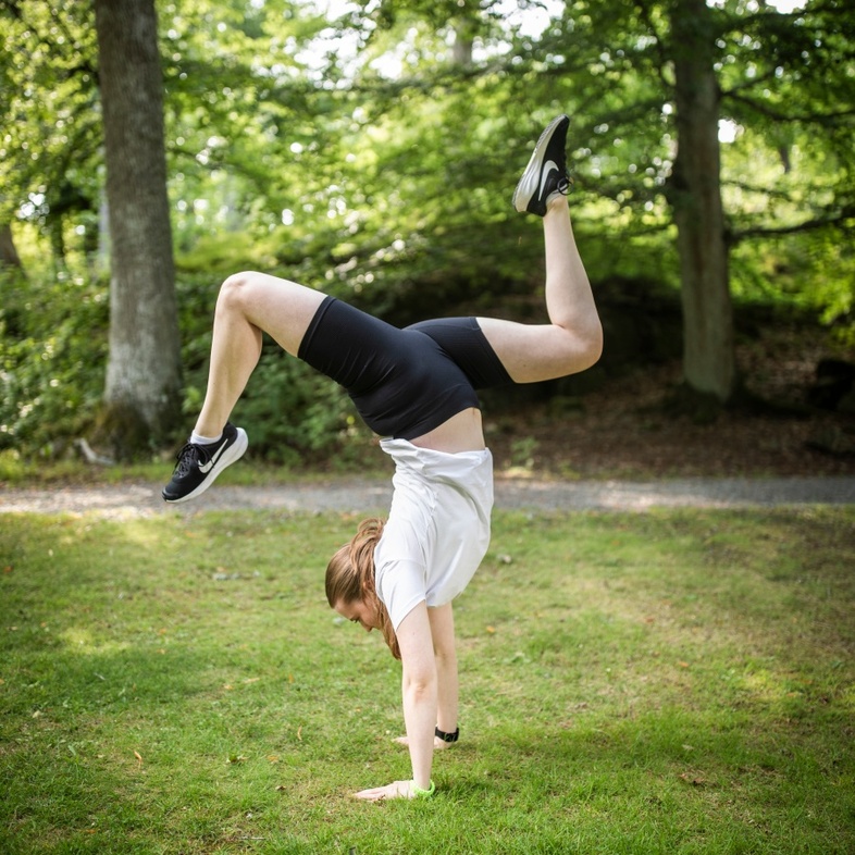 En person gör en handvolt på gräset i en grönskande park.
