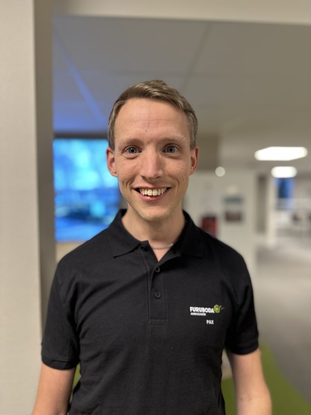 Leende man i svart pikétröja står inomhus i en ljus kontorsmiljö.