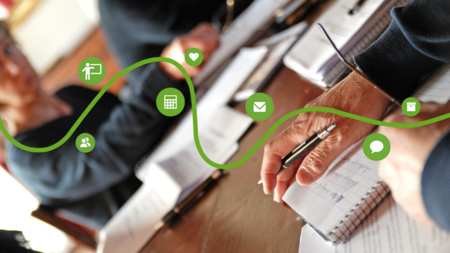 Personer skriver i anteckningsböcker vid ett bord, med gröna ikoner och en vågig linje ovanpå bilden.