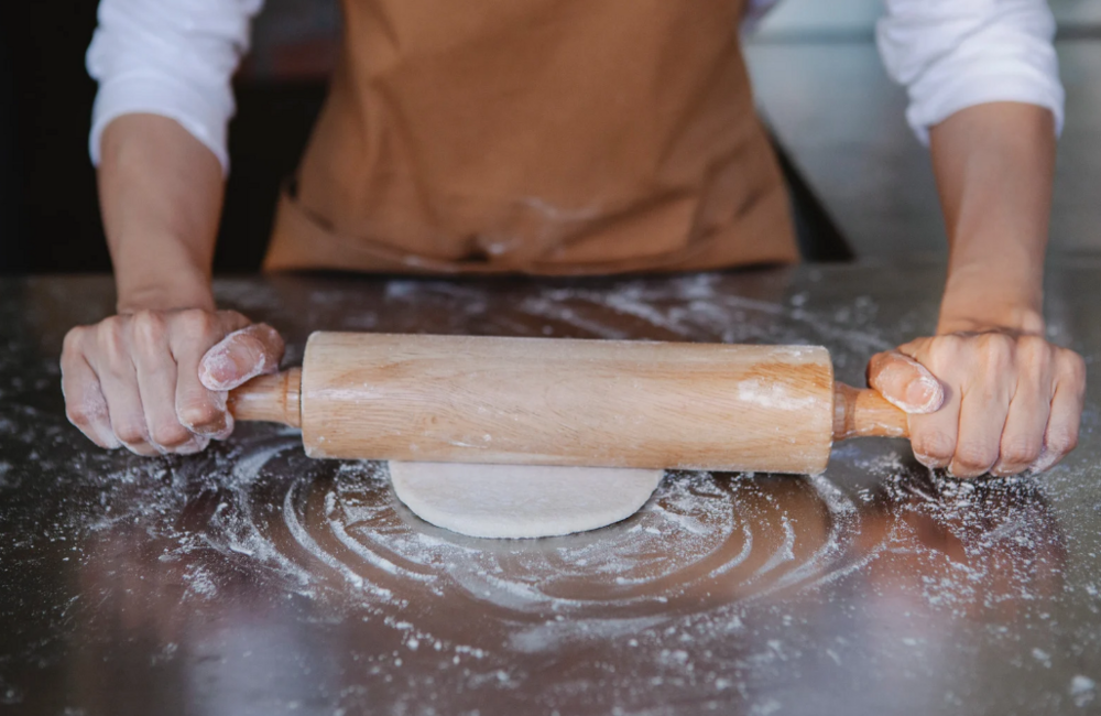Person kavlar ut deg med en träkavel på ett mjölat bord.