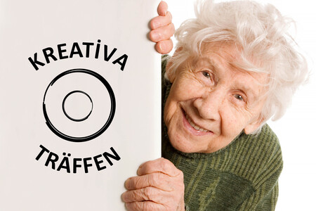 Leende äldre kvinna i grön tröja håller i en skylt med texten 'Kreativa träffen' och en cirkelgrafik.
