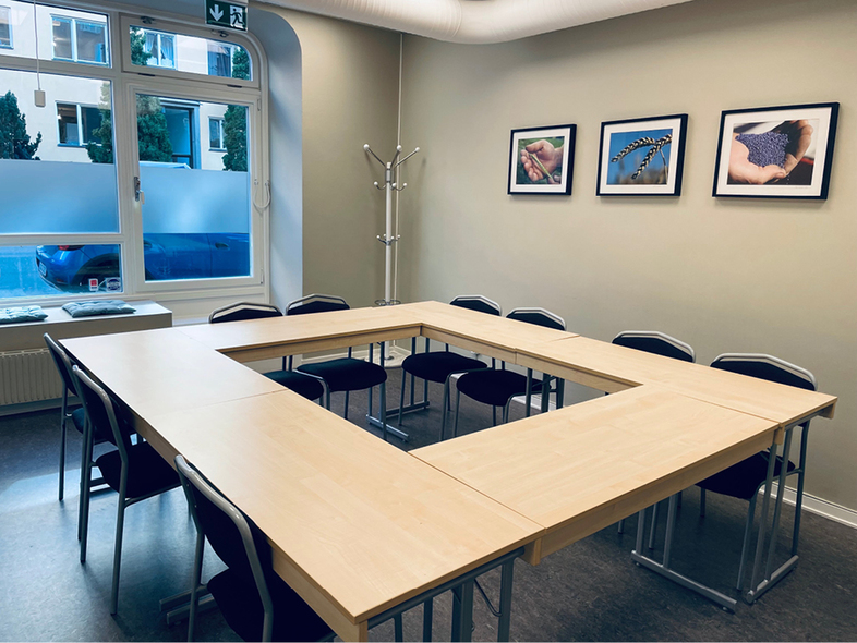 Ett ljust konferensrum med U-format bord, svarta stolar, fönster och tre tavlor på väggen.